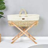 Little Green Sheep Moses Basket Stand pictured in a room with a grey coloured wall. A moses basket with a knitted insert is on the stand