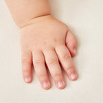 A close up of a baby's hand on a Little Green Sheep Organic Moses Basket / Pram Mattress Protector