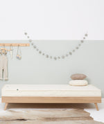 A wooden trundle bed with a Little Green Sheep atress on it. The bed is in a bedroom with walls painted white and light green.