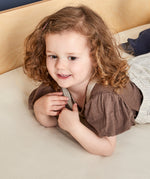 Child lying on linen colour Little Green Sheep Organic Cot & Cot Bed Fitted Sheet