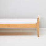 Little Green Sheep Organic Single Jersey Fitted Sheet pictured on a mattress on a wooden bed