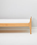 Little Green Sheep Organic Single Jersey Fitted Sheet pictured on a mattress on a wooden bed