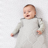 A baby lying on a rice print bed sheet wearing a dove rice print slepping bag