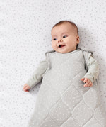 A baby lying on a rice print bed sheet wearing a dove rice print slepping bag