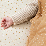 A close up of the popper closure detail underneath a baby's arm on the Little Green Sheep Organic Baby Sleeping Bag 2.5 Tog in Honey Rice print