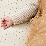 A close up of the popper closure detail underneath a baby's arm on the Little Green Sheep Organic Baby Sleeping Bag 2.5 Tog in Honey Rice print