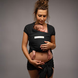 A mother wearing her baby in a black coloured Love Radius Basic Organic Baby Wrap. Babipur stock a wide range of organic baby wraps and carriers. 