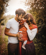 Two parents standing next to each other. The mother is wearing her baby in a fawn coloured Love Radius Basic Organic Baby Wrap. Babipur stock a wide range of organic baby wraps and carriers in various colurs. 