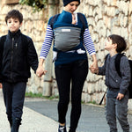 Adult carrying a baby in the Love Radius Original JPMBB Baby outside holding the hands of two younger siblings.