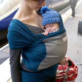 Adult carrying a baby in the Love Radius Original JPMBB Baby Wrap - peacock blue/elephant at a train station