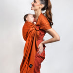 A parent wearing their young baby in a fawn orange coloured Love Radius No Knot Woven Wrap. A wide range of baby wraps and carriers are available at Babipur. 