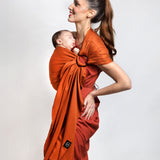 A parent wearing their young baby in a fawn orange coloured Love Radius No Knot Woven Wrap. A wide range of baby wraps and carriers are available at Babipur. 