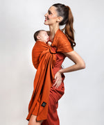A parent wearing their young baby in a fawn orange coloured Love Radius No Knot Woven Wrap. A wide range of baby wraps and carriers are available at Babipur. 