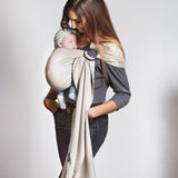 A parent wearing their baby in a white gold coloured Love Radius No Knot Woven Wrap. A wide range of baby wraps and carriers are available at Babipur. 