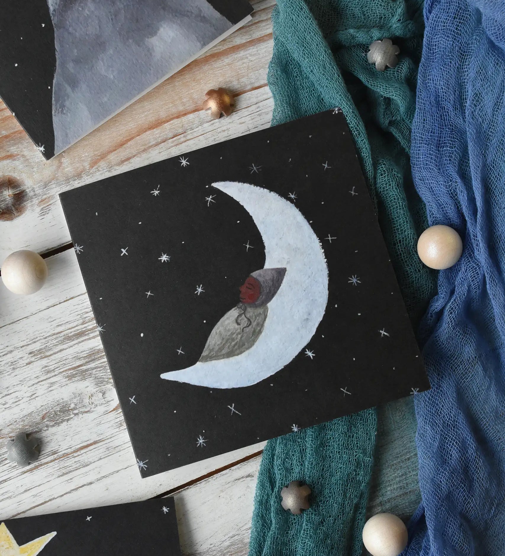 LydiaMae moon baby greetings card placed in a flatlay with Ostheimer play cloths and pieces from the Grapat dear universe play set.