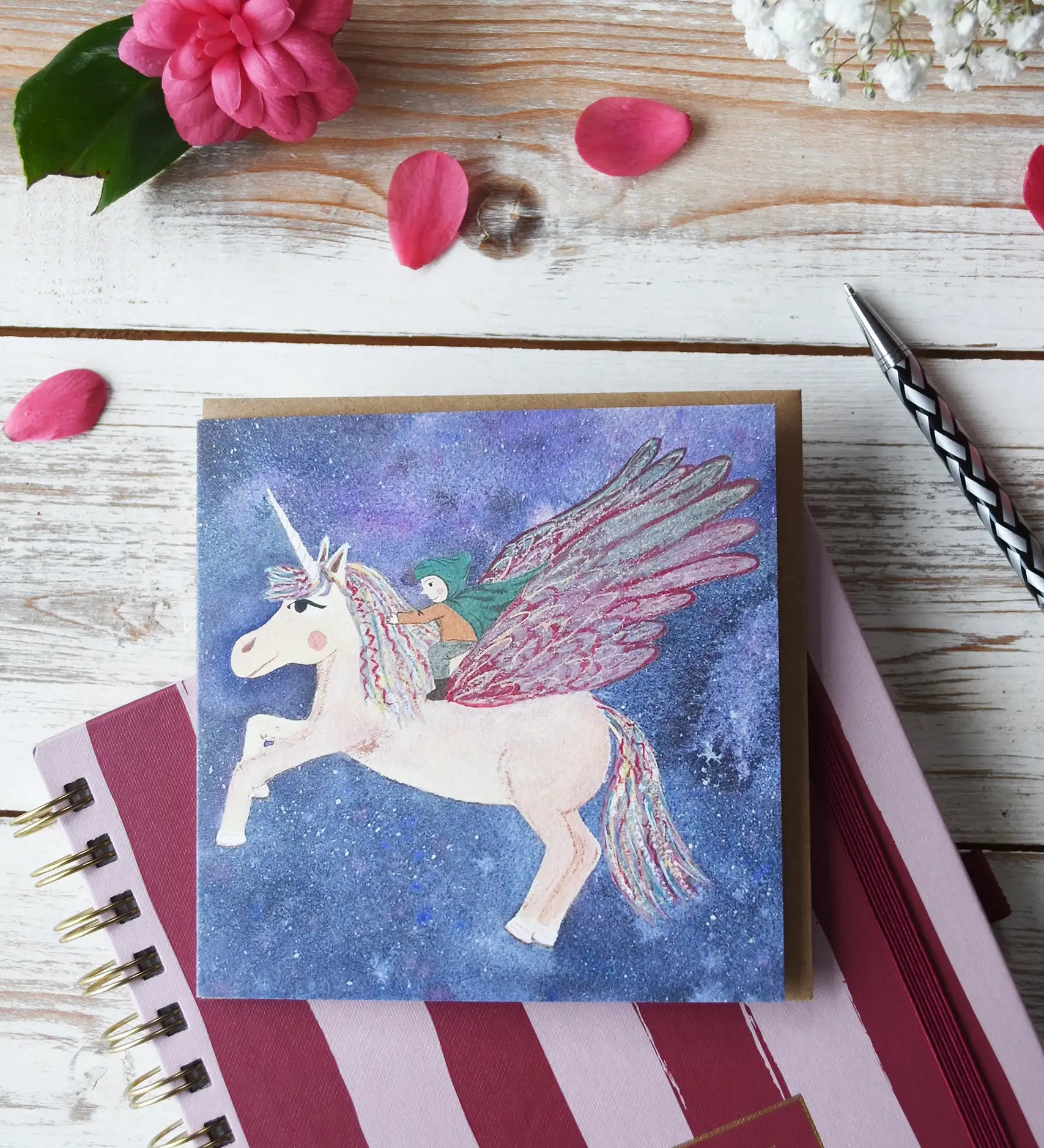 LydiaMae Pegasus Greetings Card placed on top of a striped diary next to a writing pen.