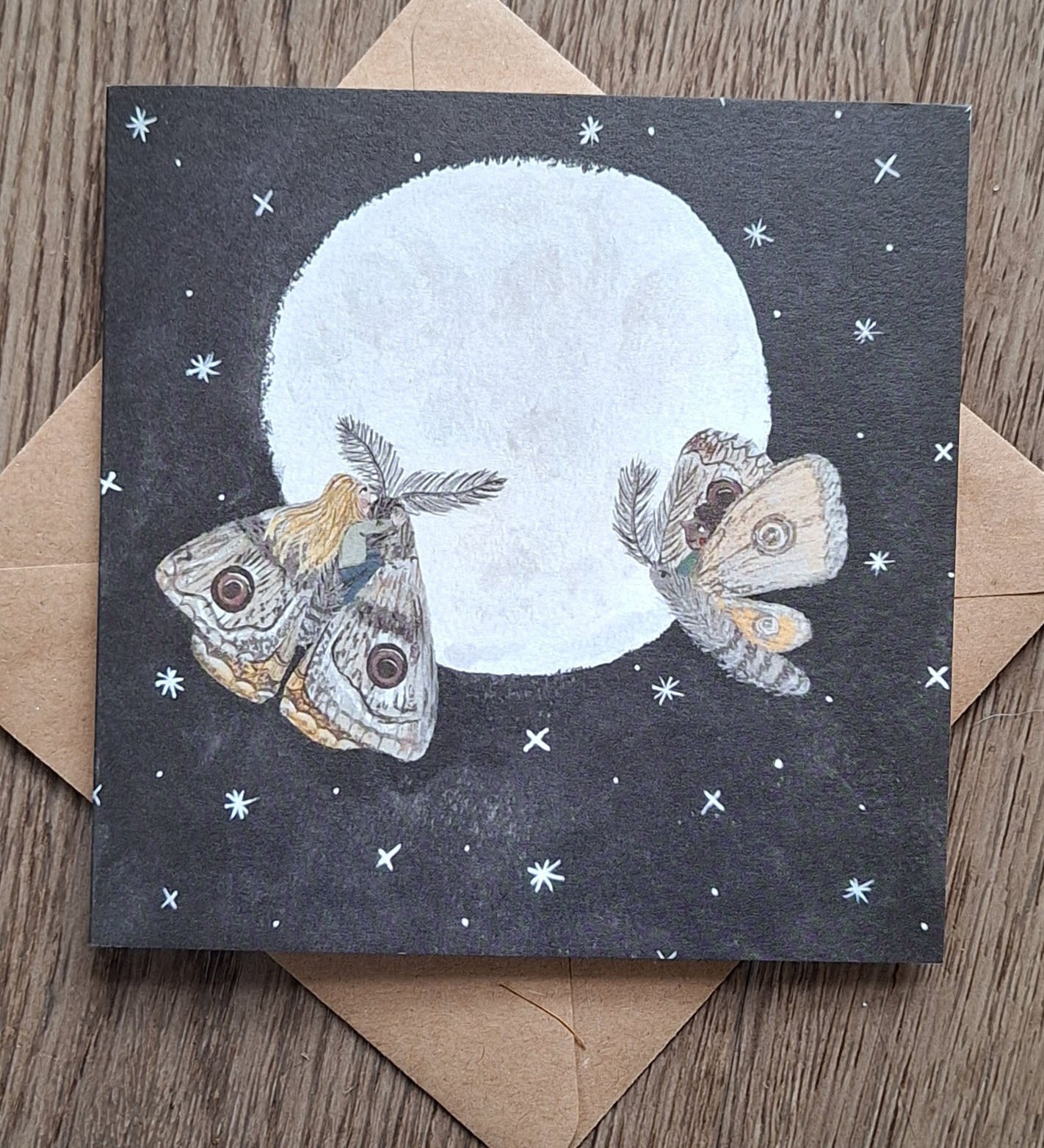 Moths in the moonlight greetings card from Lydiamae showing a drawing of two moths in front of the moon in a soft drawing style. Card is on top of a brown envelope