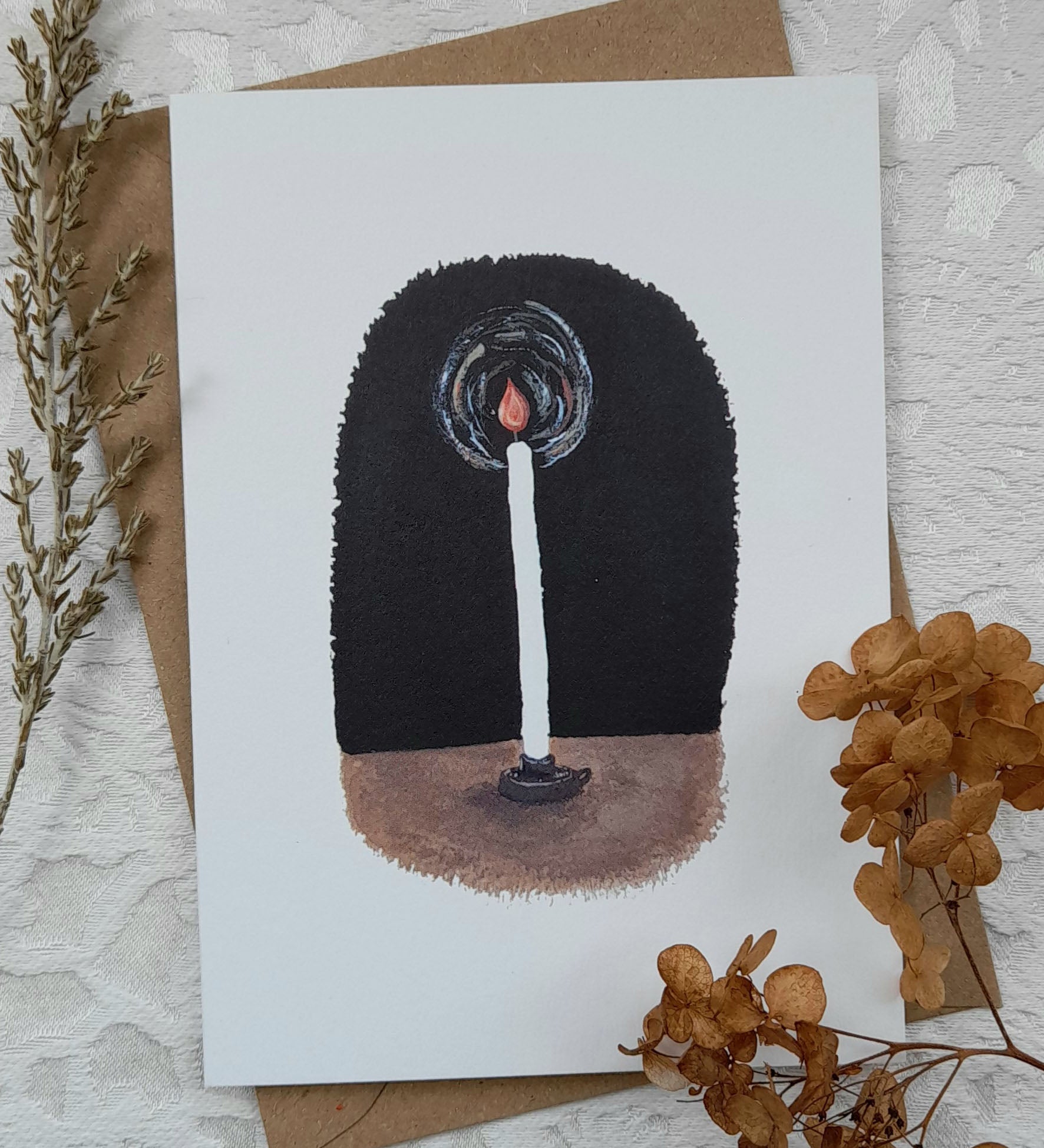 Simple candle greetings card from Lydiamae showing a illustration of a lit candlestick in a soft drawing style. Card is on top of a brown envelope