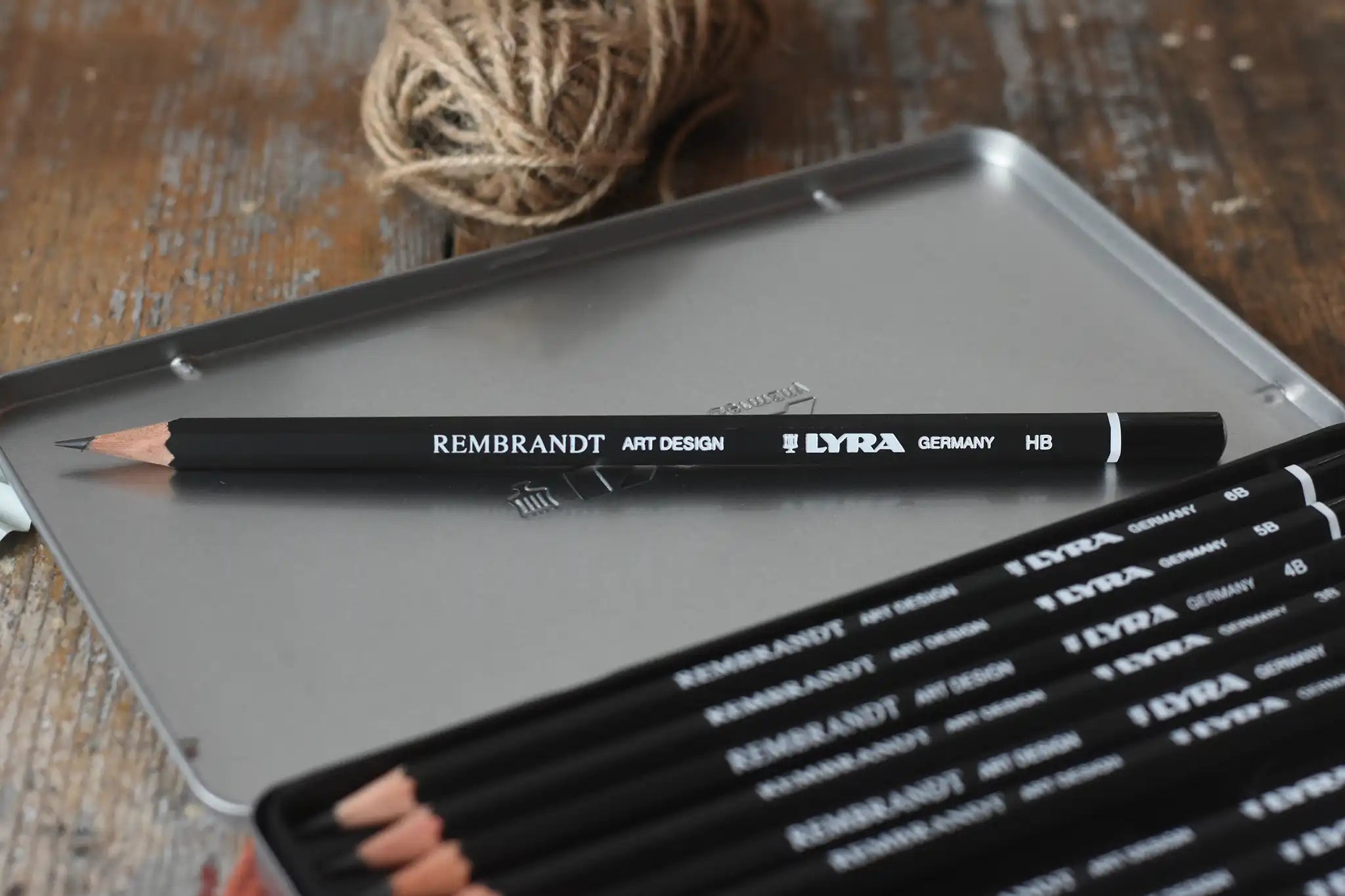 Close up of Lyra 12 drawing pencils in sizes from 6B to 4H in a metal storage tin.