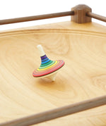 Rainbow stripe rallye spinning top on the Mader Kreiselmanufaktur Manège wooden spinning plate.