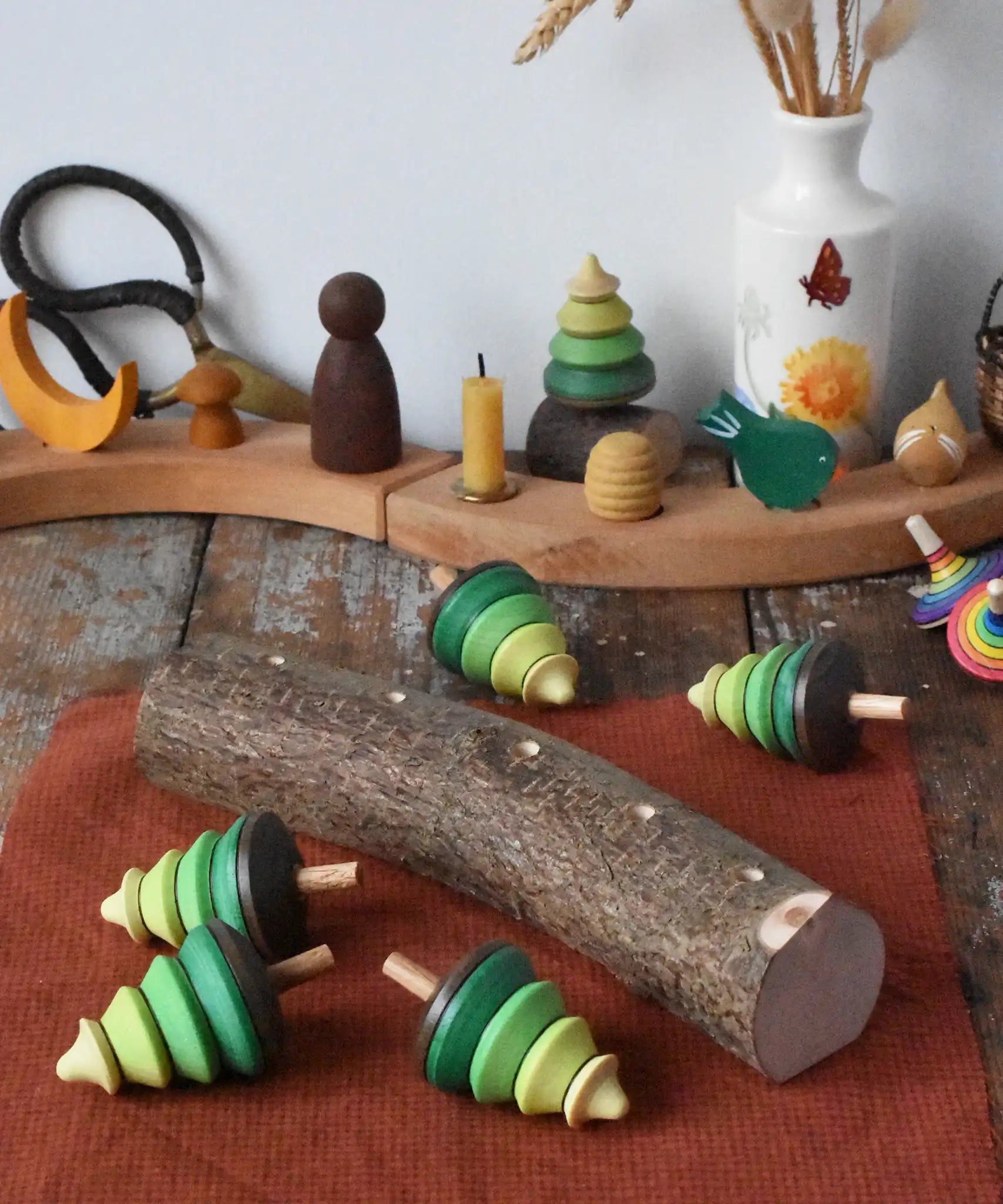 Mader Kreiselmanufaktur 5 tree spinning tops on branch placed on a wooden desk in the Babipur playroom. The trees have all been taken out of the slots and placed besides the branch.