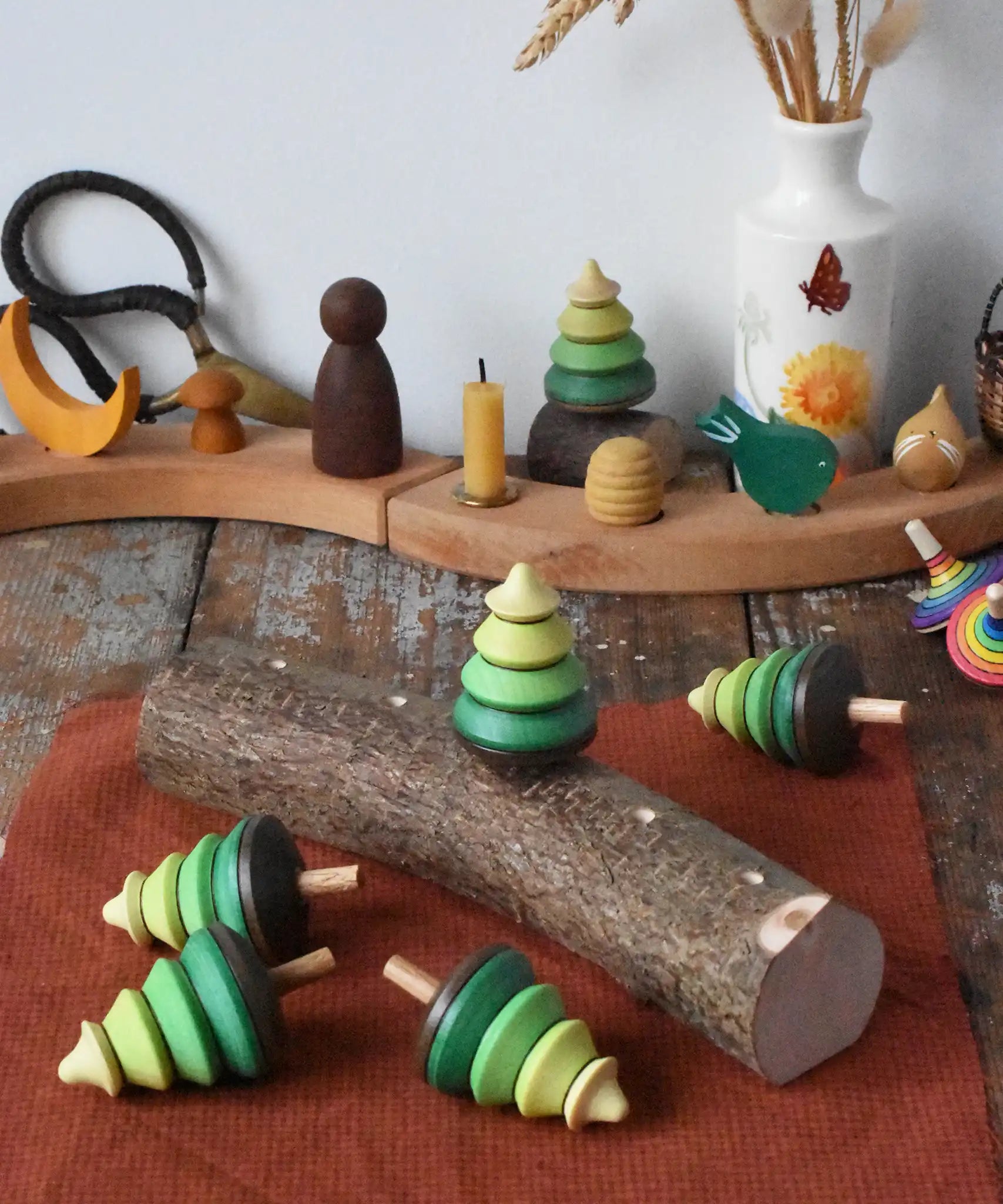 Mader Kreiselmanufaktur 5 tree spinning tops on branch placed on a wooden desk in the Babipur playroom. One is slotted into the branch the others have been laid besides it.