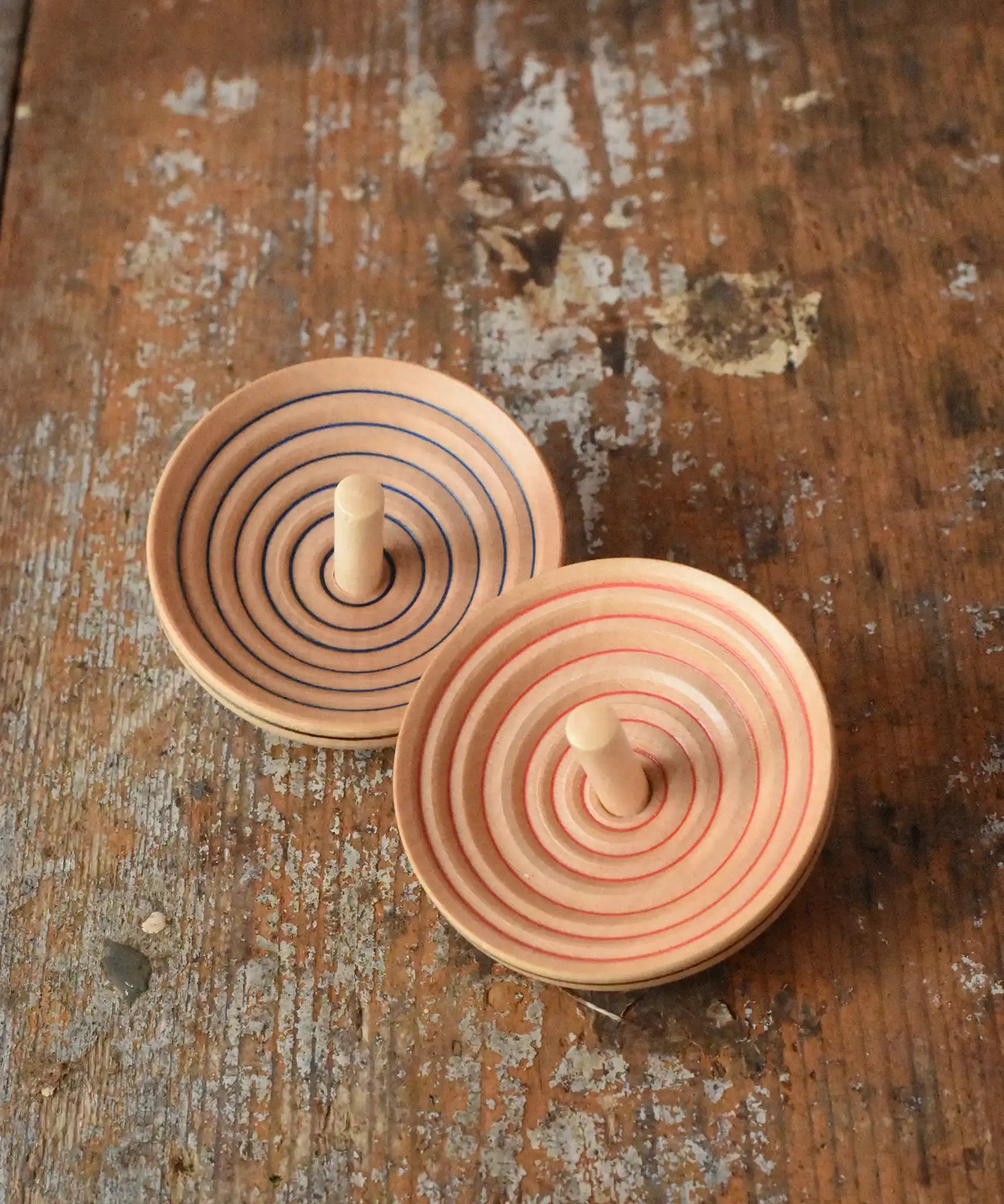 Two Mader UFO campanola spinning top in blue and red placed on a wooden desk in the Babipur playroom. 