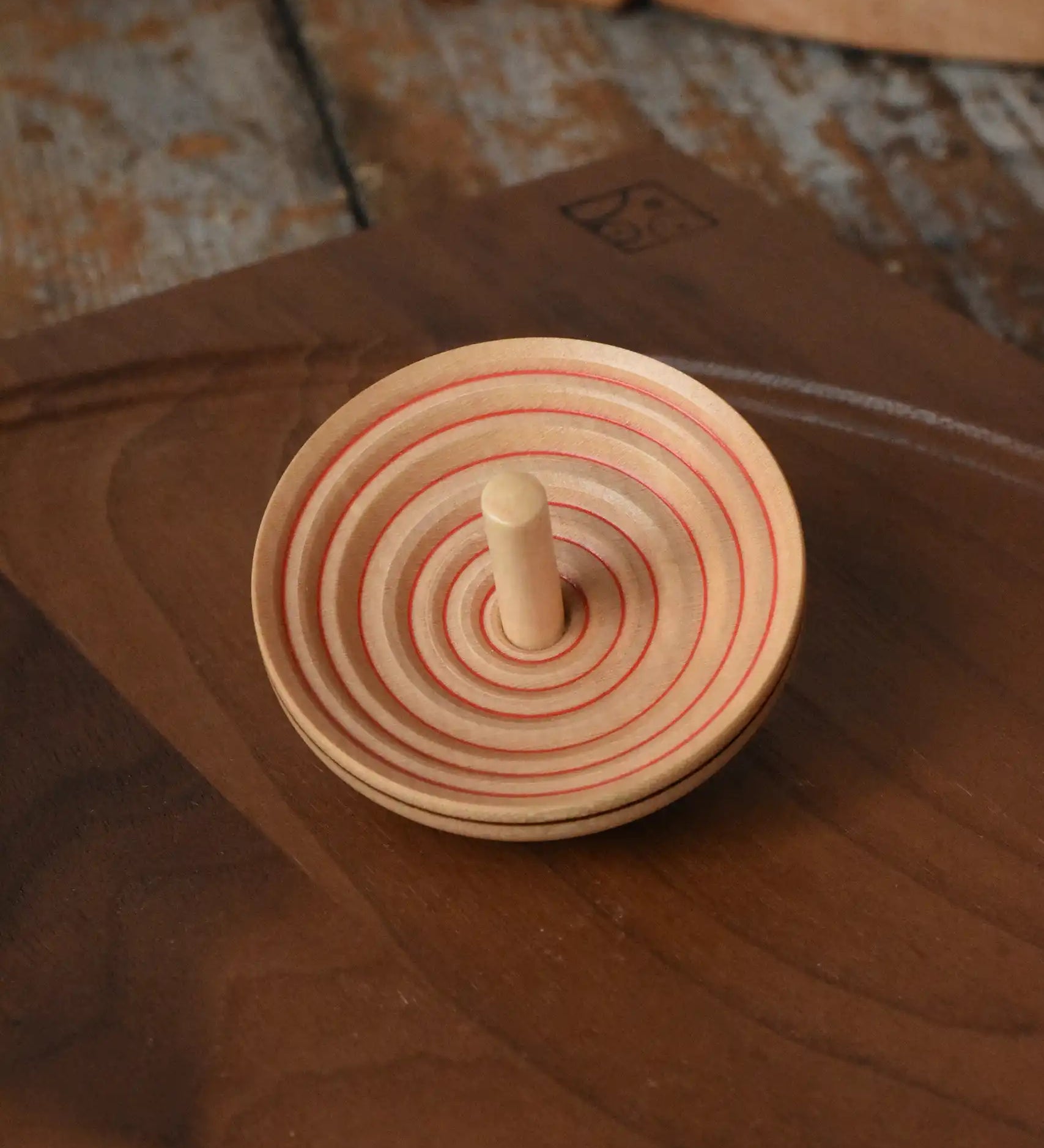 Mader UFO campanola spinning top in red placed on a walnut wood spinning plate.