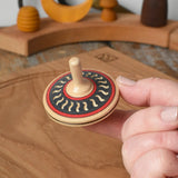 Mader Kreiselmanufaktur arabesk wooden finger spinning top shown balanced on an adult's finger in the Babipur playroom.