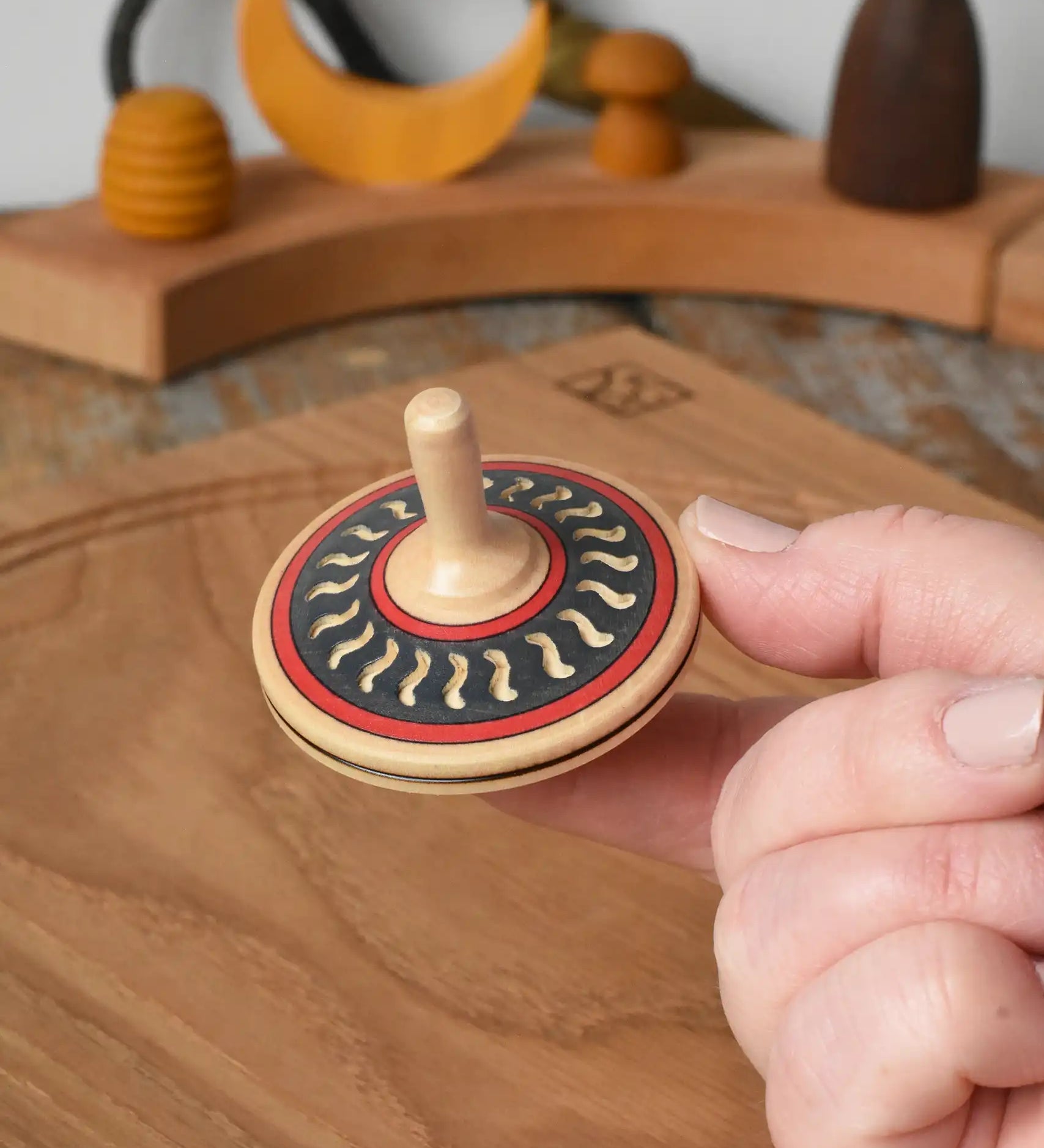 Mader Kreiselmanufaktur arabesk wooden finger spinning top shown balanced on an adult's finger in the Babipur playroom.