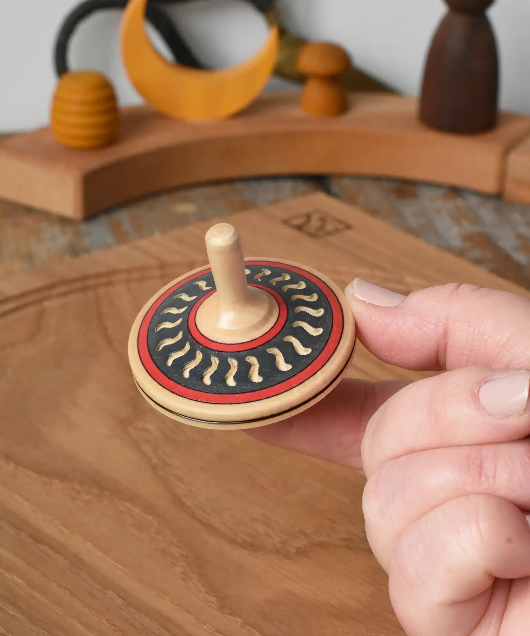Mader Kreiselmanufaktur arabesk wooden finger spinning top shown balanced on an adult's finger in the Babipur playroom.