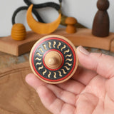 Mader Kreiselmanufaktur arabesk wooden finger spinning top held in an adult's hand.
