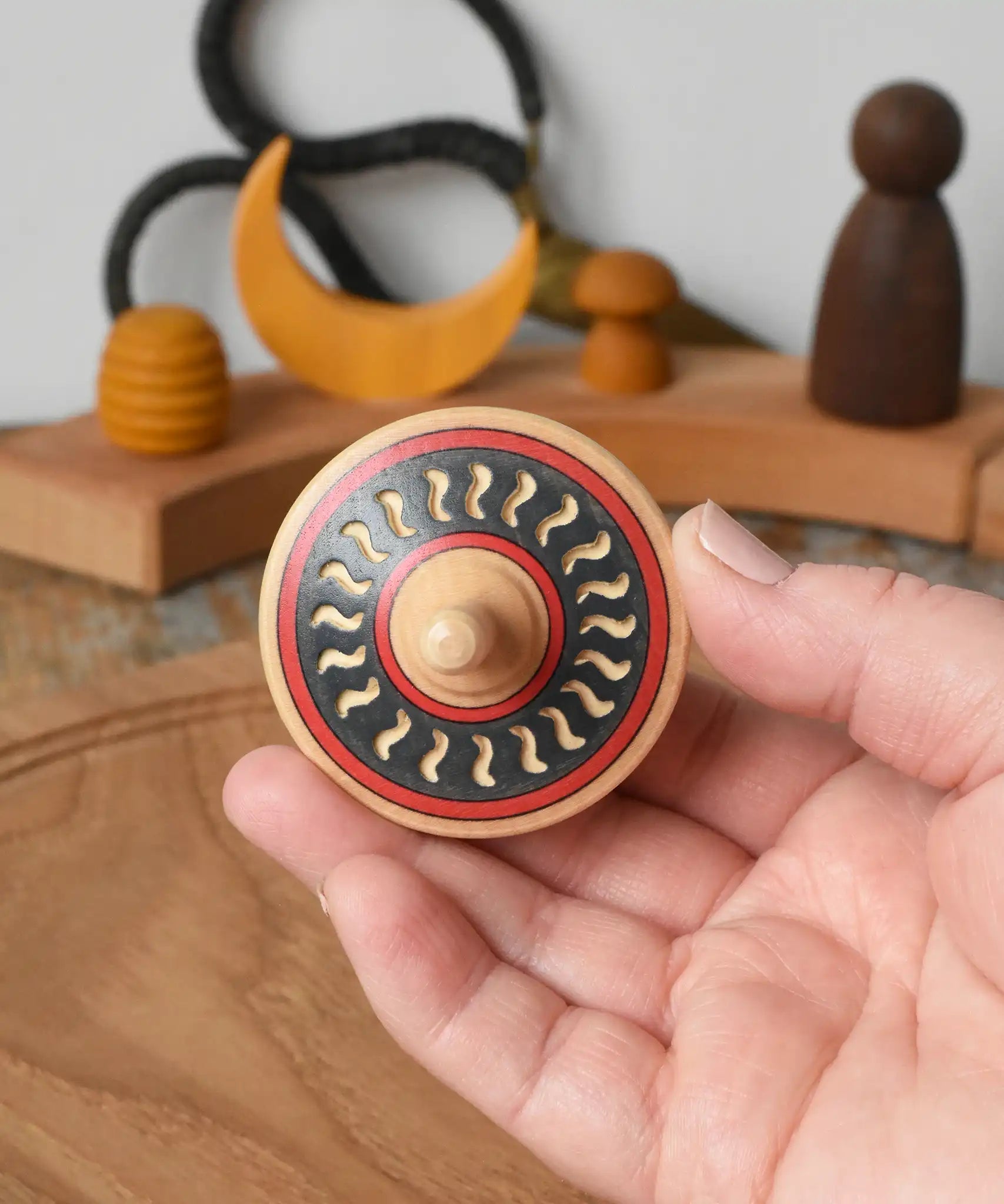 Mader Kreiselmanufaktur arabesk wooden finger spinning top held in an adult's hand.