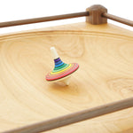 Close up of a Mader Rainbow stripe spinning toy on a Mader large wooden spinning plate