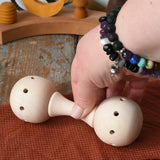 Mader Kreiselmanufaktur traditional wooden baby rattle placed on a cloth on a wooden surface in the Babipur playroom. An adult's hand can be seen picking the toy rattle up.
