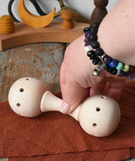 Mader Kreiselmanufaktur traditional wooden baby rattle placed on a cloth on a wooden surface in the Babipur playroom. An adult's hand can be seen picking the toy rattle up.