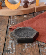 Mader hexagon 8cm spinning top plate in black oak placed on a wooden surface in the Babipur playroom.
