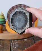 Mader hexagon 8cm spinning top plate in black oak in an adult's hand
