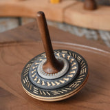 Mader Kreiselmanufaktur bonbon wooden spinning top in black placed on a walnut wood spinning plate in the Babipur playroom.