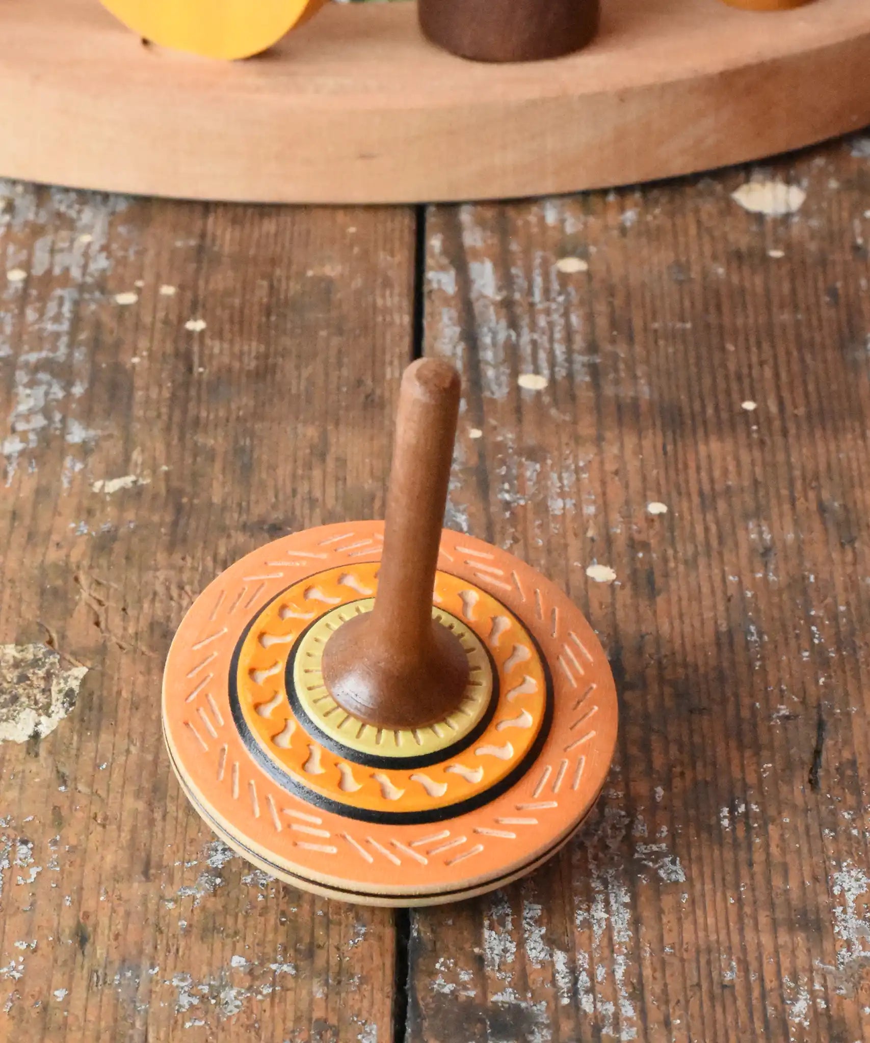 Orange Mader Kreiselmanufaktur bonbon wooden spinning top placed on a wooden desk in the Babipur playroom.