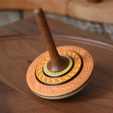 Mader Kreiselmanufaktur bonbon wooden spinning top in orange placed on a walnut wood spinning plate in the Babipur playroom.