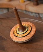 Mader Kreiselmanufaktur bonbon wooden spinning top in orange placed on a walnut wood spinning plate in the Babipur playroom.