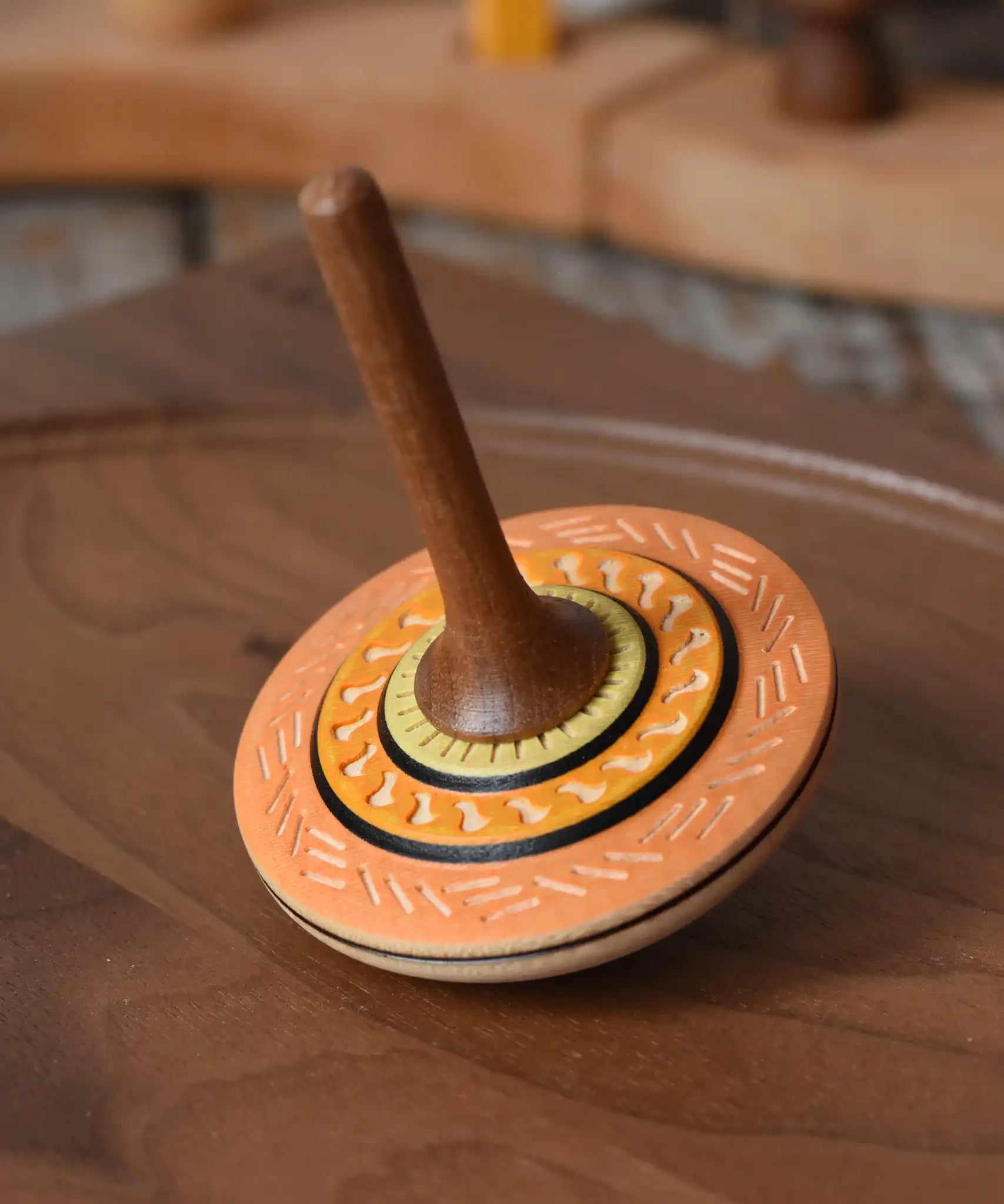 Mader Kreiselmanufaktur bonbon wooden spinning top in orange placed on a walnut wood spinning plate in the Babipur playroom.