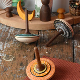 Three Mader Kreiselmanufaktur bonbon wooden spinning tops placed on a wooden desk in the Babipur playroom.
