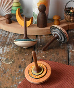 Three Mader Kreiselmanufaktur bonbon wooden spinning tops placed on a wooden desk in the Babipur playroom.