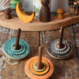 Three Mader Kreiselmanufaktur bonbon wooden spinning tops placed on a wooden desk in the Babipur playroom.