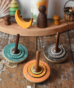 Three Mader Kreiselmanufaktur bonbon wooden spinning tops placed on a wooden desk in the Babipur playroom.