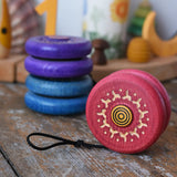 Mader burlesk wooden yoyo in pink placed on a wooden surface in the Babipur playroom. Other colours of the yoyo can be seen in the background.