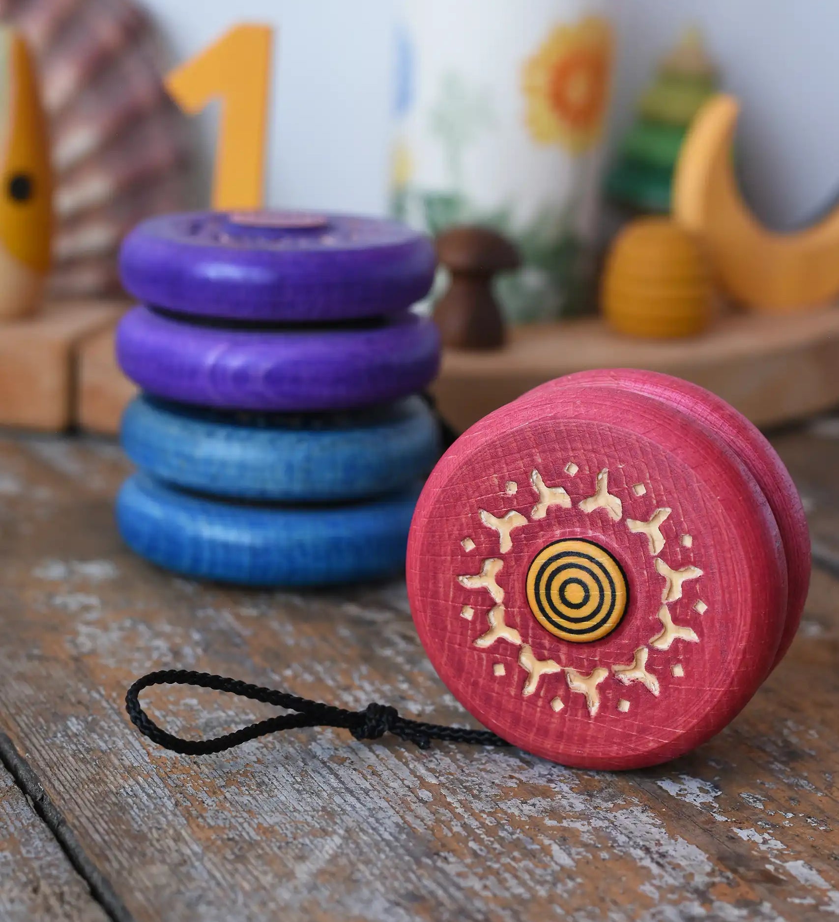Mader burlesk wooden yoyo in pink placed on a wooden surface in the Babipur playroom. Other colours of the yoyo can be seen in the background.