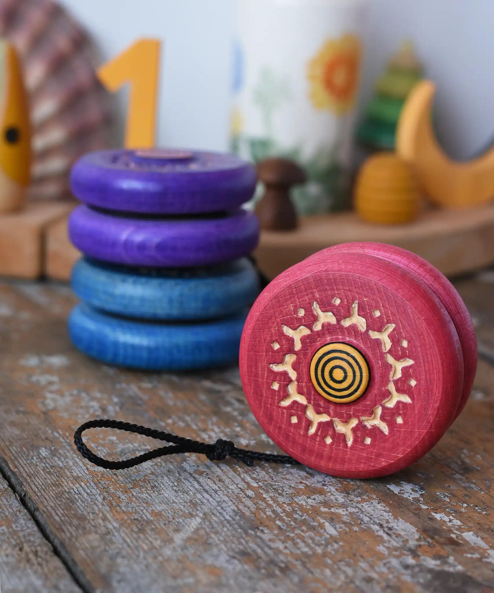 Mader burlesk wooden yoyo in pink placed on a wooden surface in the Babipur playroom. Other colours of the yoyo can be seen in the background.